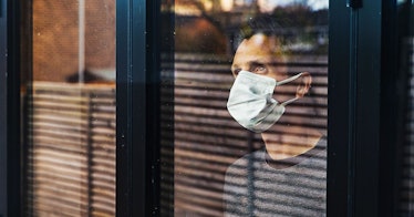 A man with his mask on looks outside a window