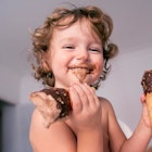 一个婴儿一手拿着一个巧克力冰淇淋甜筒，把巧克力冰淇淋涂在他们的脸上。
