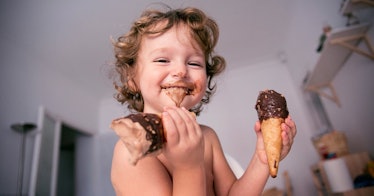 A baby holds a chocolate ice cream cone in each hand and has chocolate ice cream smeared on their fa...