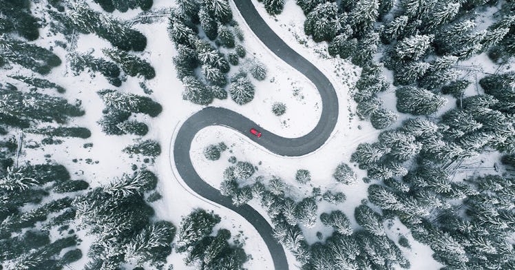 A red car driving on a road in the middle of a mountain full of snow
