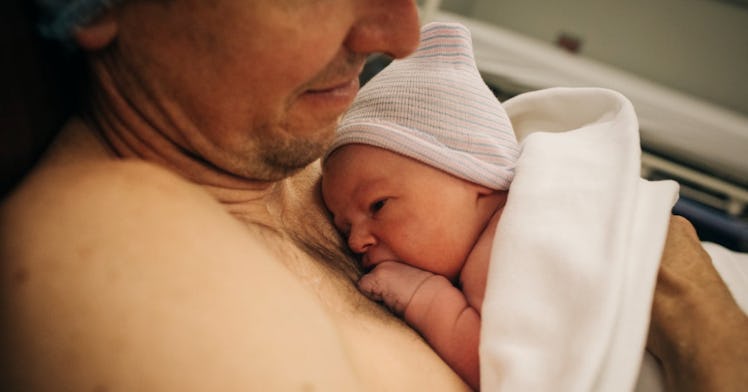 A shirtless father holds his newborn to his chest.