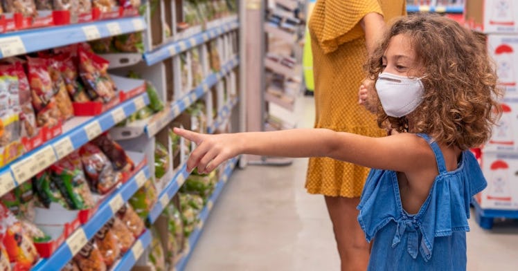 A little girl points at a product in a store with an N95 face mask on