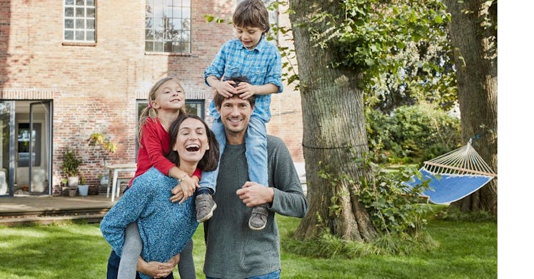 a family of four stands in front of. house in a yard and laughs and smiles