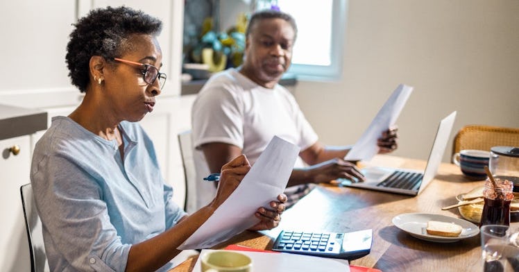 An elderly couple sit at a kitchen table and look over their finances
