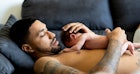 一个光着膀子的新爸爸抱着他赤裸的孩子躺在沙发上。