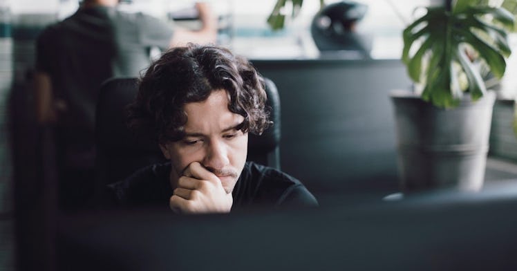 Man with long hair sitting at computer thinking