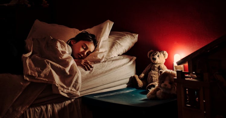 A girl sleeps in bed with a night light on.