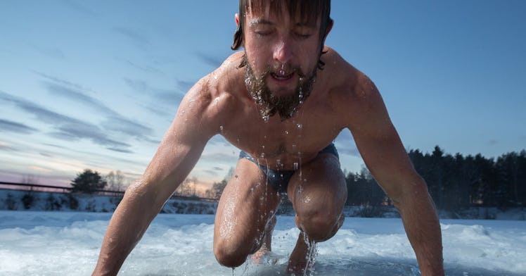 A wet, shirtless man leans over an ice hole.