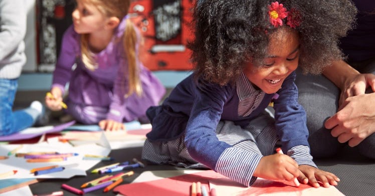 a young Black girl draws with crayon, while smiling