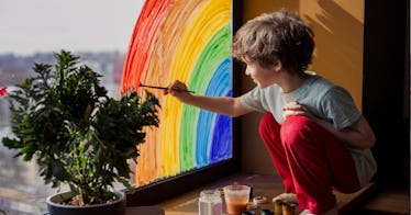 creative young boy painting rainbow on window