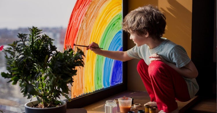creative young boy painting rainbow on window