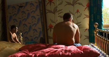 一个光着膀子的男人坐在床上，镜子里倒映着他的形象。