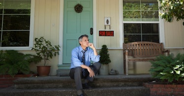 a man sits in front of his house that is being sold due to foreclosure