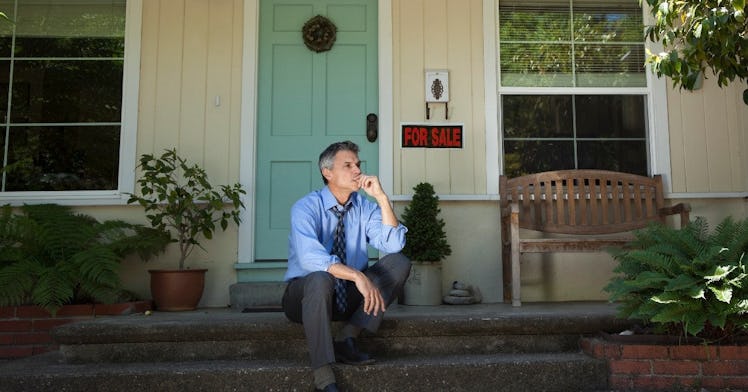 a man sits in front of his house that is being sold due to foreclosure