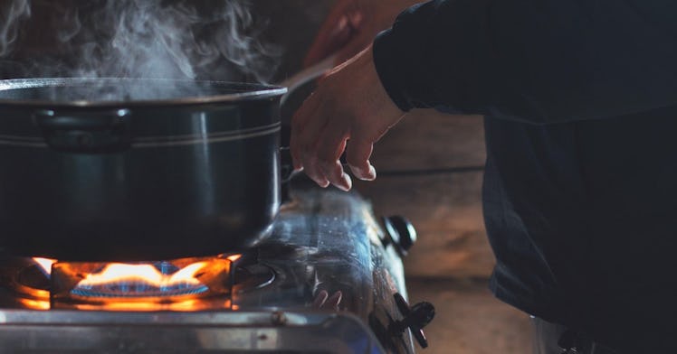 a man stands over a gas stove that is heating up a dutch oven