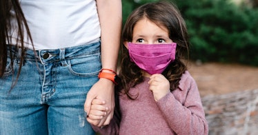 A young girl wearing a mask holds her mother's hand.
