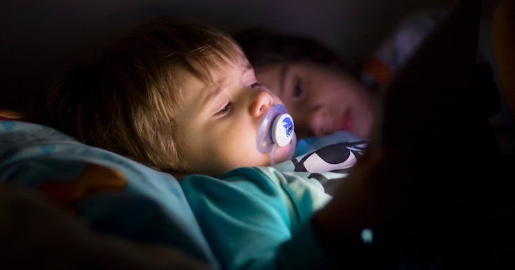 A toddler with a pacifier looks at a tablet screen.