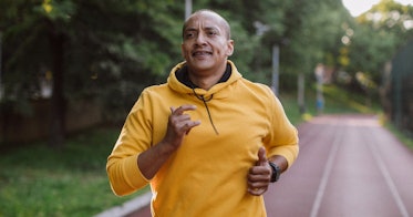 A man runs on a road surrounded by trees.