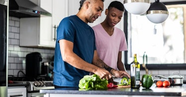 A father and a son cook fresh vegetables in olive oil in a kitchen