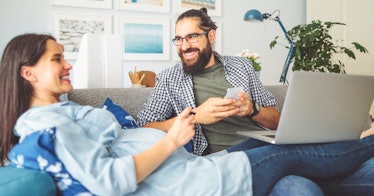 a couple, woman pregnant, on couch together and looking at finances while smiling
