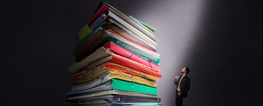 The large amount of work accumulated after paternity leave with a large stack of folders piled up an...
