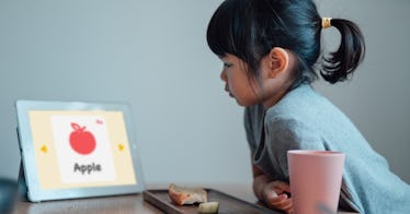 A little girl stares at an iPad learning the word Apple over lunch.