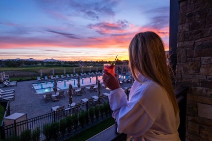 A woman with a cocktail looking at a sunset at Pronghorn Resort