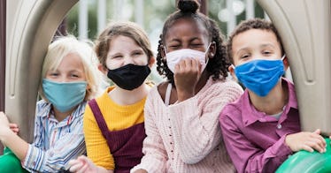 four children sit on a playground while each wearing a face mask