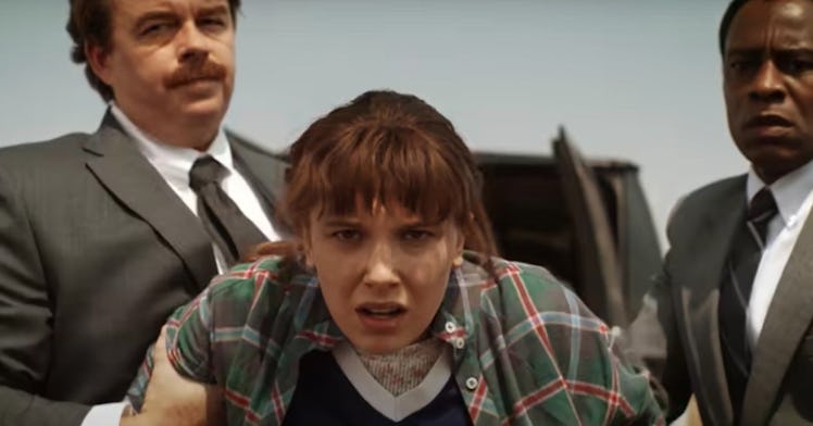Eleven is being held by two suited men in a Stranger Things screenshot