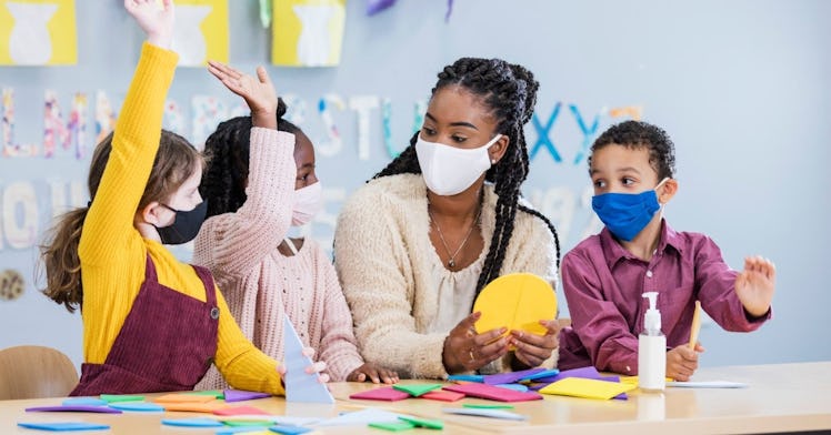 a Black woman teacher sits with three students, educating them