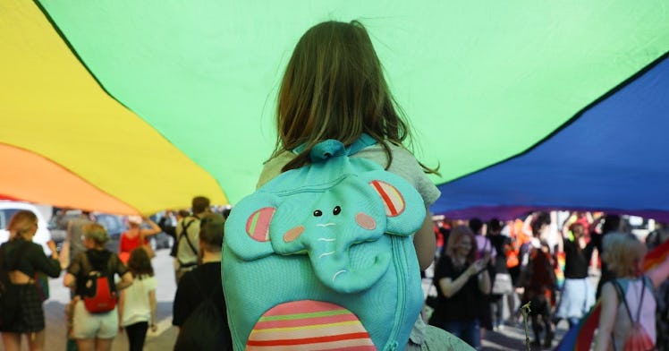 a little kid on a parents shoulders walks underneath a massive pride-colored piece of fabric