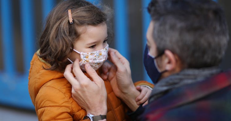 A dad wearing a mask puts a mask on his daughter.