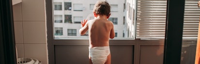 A baby in a diaper stares out a window.