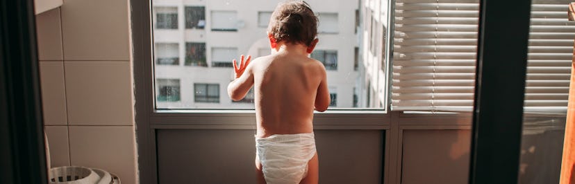 A baby in a diaper stares out a window.