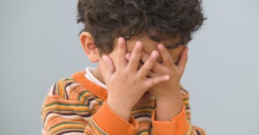 A child covers their face with their hands.
