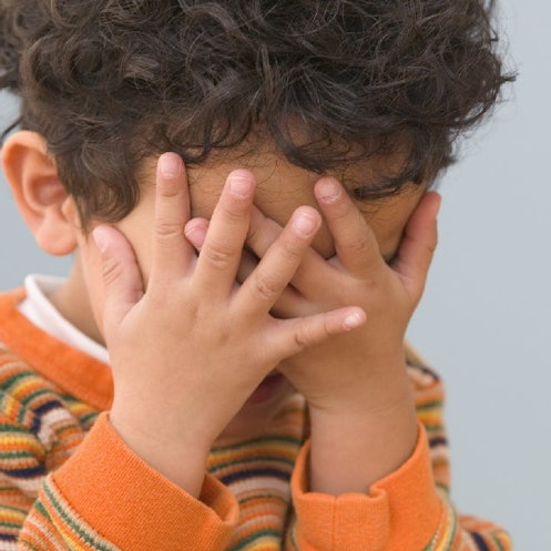 A child covers their face with their hands.