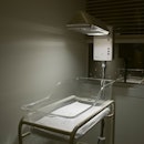 a warming bassinet sits empty in a dark corner of a hospital room