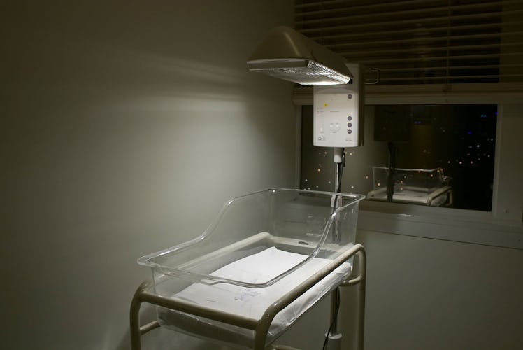a warming bassinet sits empty in a dark corner of a hospital room