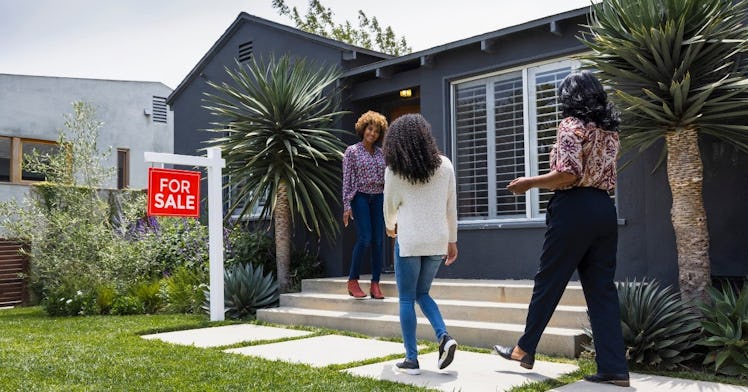 a daughter and mom walk up to a real estate agent in front of a house on sale