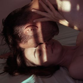 Couple touching foreheads in bed with light casting on them