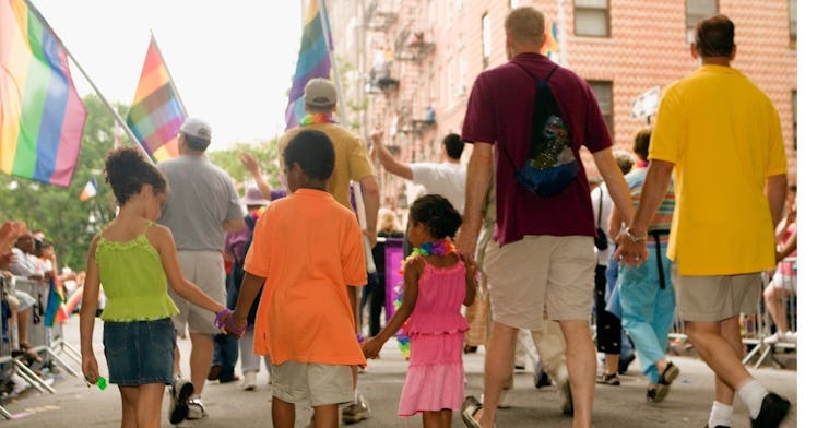 a few kids and two adults hold hands at a LGBTQ+ pride parade