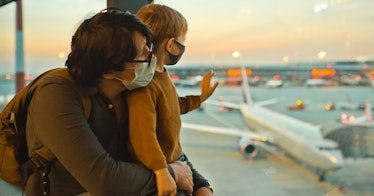 a dad and his son look out an airport window with masks on