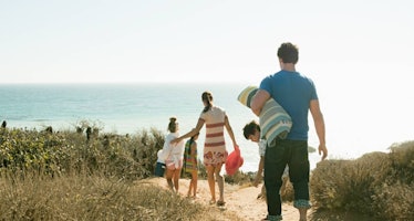Family walking towards ocean with towels and beach gear in hand