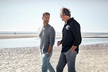 Two middle aged men talking as they walk along the beach