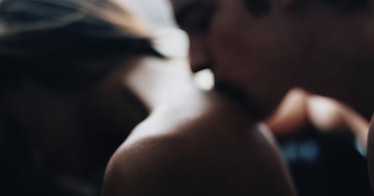 slightly blurred image of a man kissing a woman's naked shoulder from behind