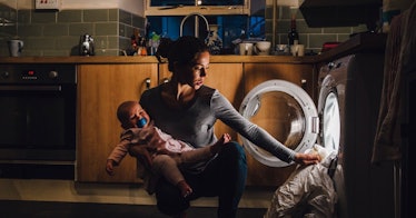 a mom takes a duvet out of the washing machine while holding a baby in darkness