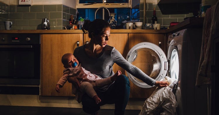 a mom takes a duvet out of the washing machine while holding a baby in darkness