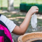 A student wearing a backpack throws away a surgical mask.