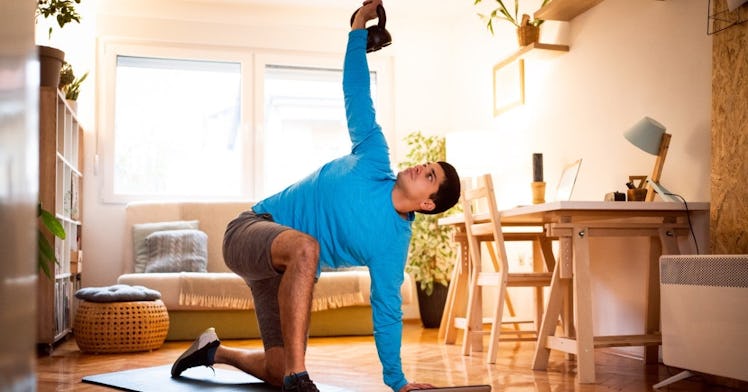 A man does a turkish get up with a kettlebell in his living room.