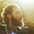 Man with beard in sunlit forest staring into the distance